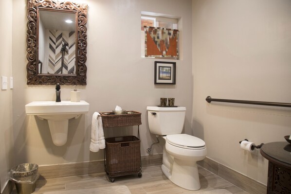 A bathroom with a white sink, toilet, and a decorative mirror. There is a wicker basket and a framed picture on the wall.