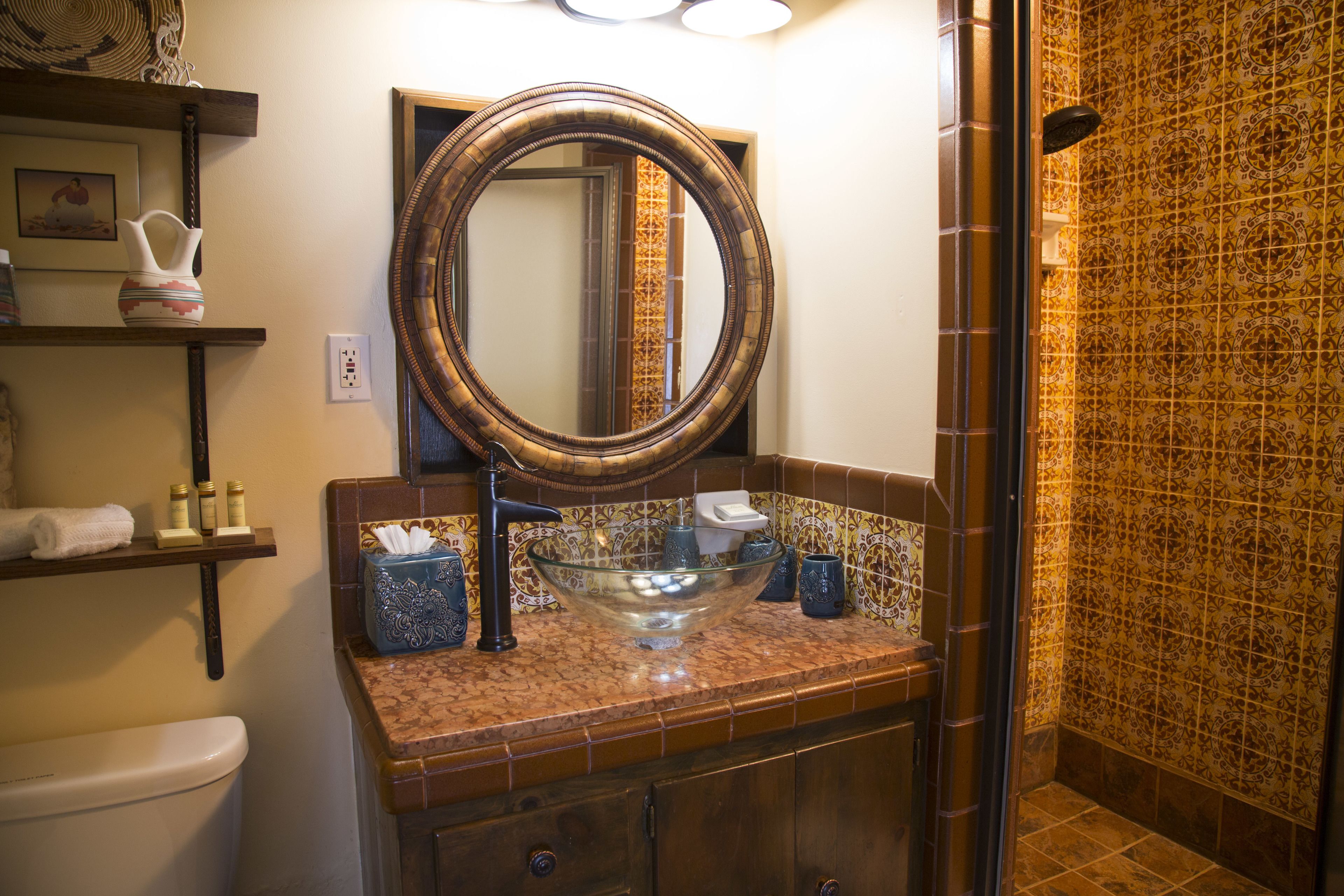 Une salle de bain dotée d’un grand miroir, d’un lavabo en verre et d’une douche aux carreaux décorés.