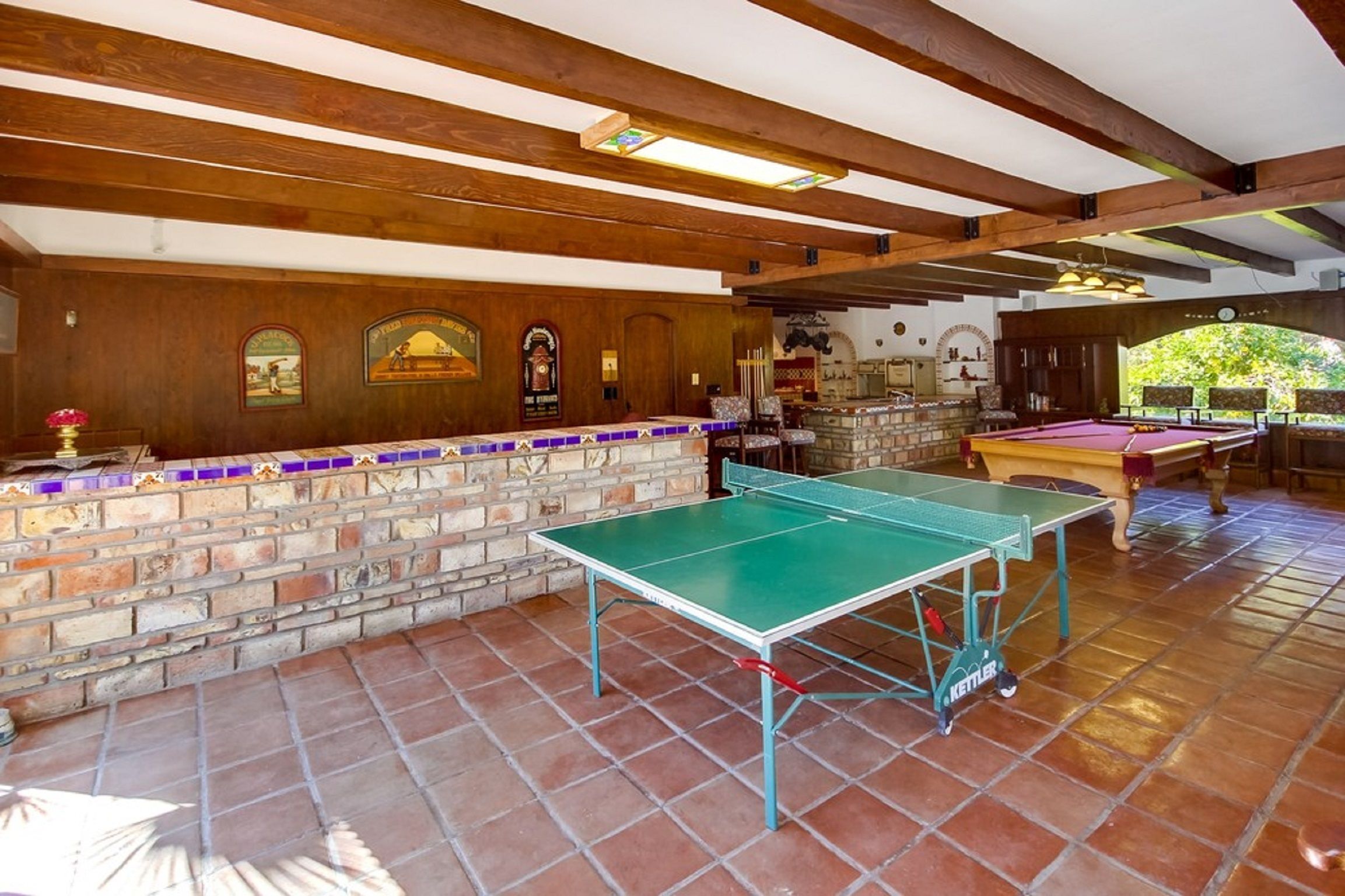 A room with a ping pong table, a pool table, and a stone wall with tiled accents.