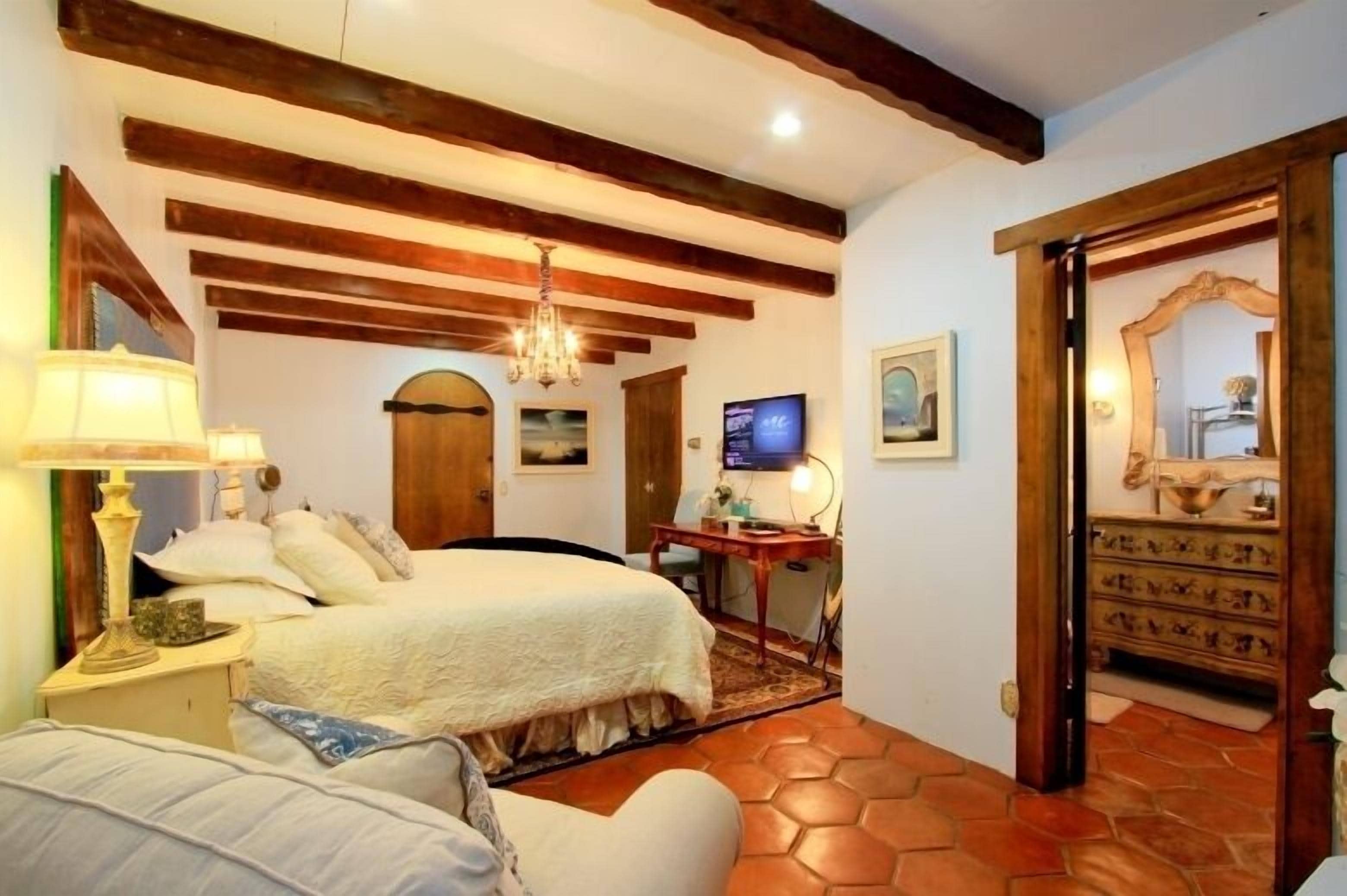 A bedroom with a bed, a desk, a television, and a mirror.