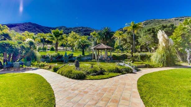 Un jardín con un pabellón, senderos y una montaña al fondo.