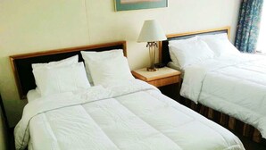 Habitación de hotel con dos camas individuales, cada una con ropa blanca y cabecero de madera. Hay una mesita de noche con lámpara entre las camas.