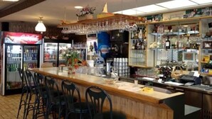 Un área de bar con mostrador de madera, taburetes, un refrigerador con bebidas y estantes llenos de botellas.