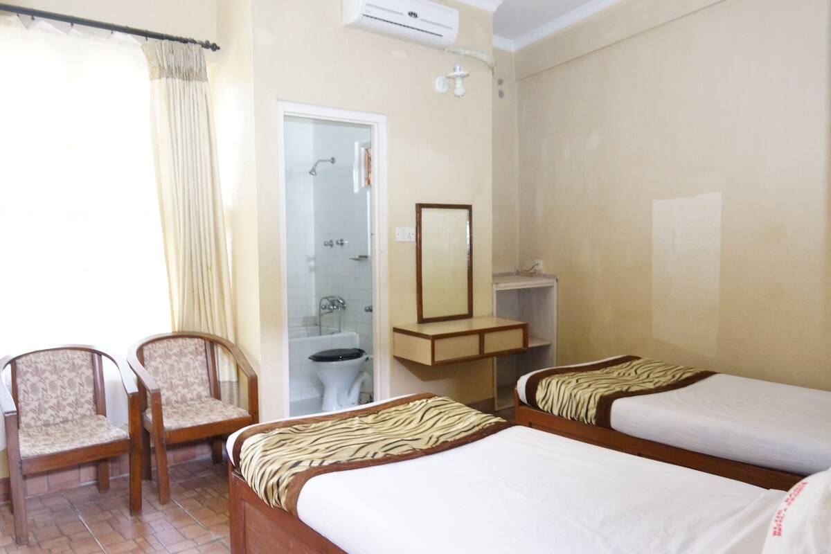 A hotel room with two beds, a bathroom, a mirror, and two chairs.