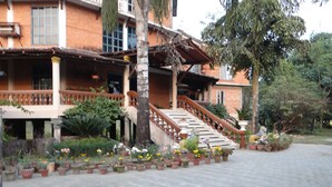 Un edificio con fachada de ladrillo, una escalera que lleva a un balcón y un jardín con plantas en macetas.