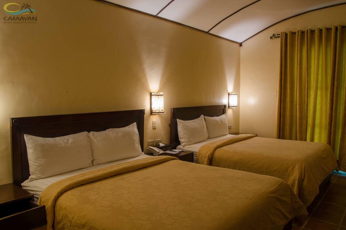 A hotel room with two beds, each with a wooden headboard, a nightstand, and a lamp.