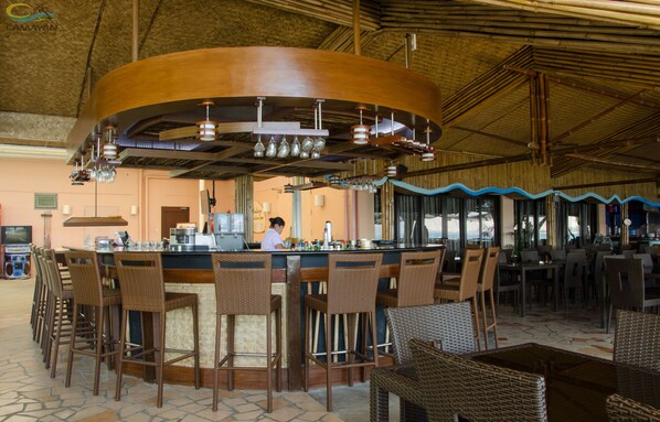 A bar area with a curved counter, wicker chairs, and a person working behind the bar. - Camayan Beach Resort (Morong)