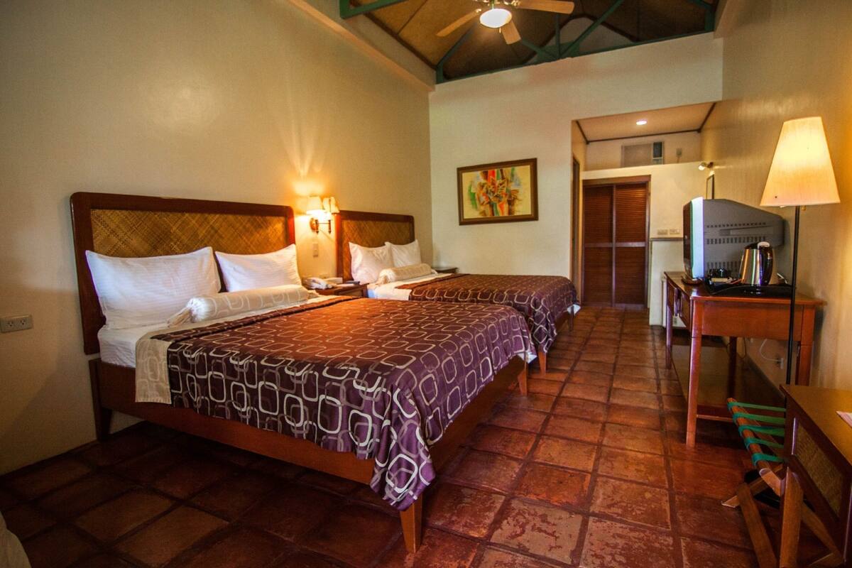 A hotel room with two beds, a desk, a chair, a television, and a painting on the wall.