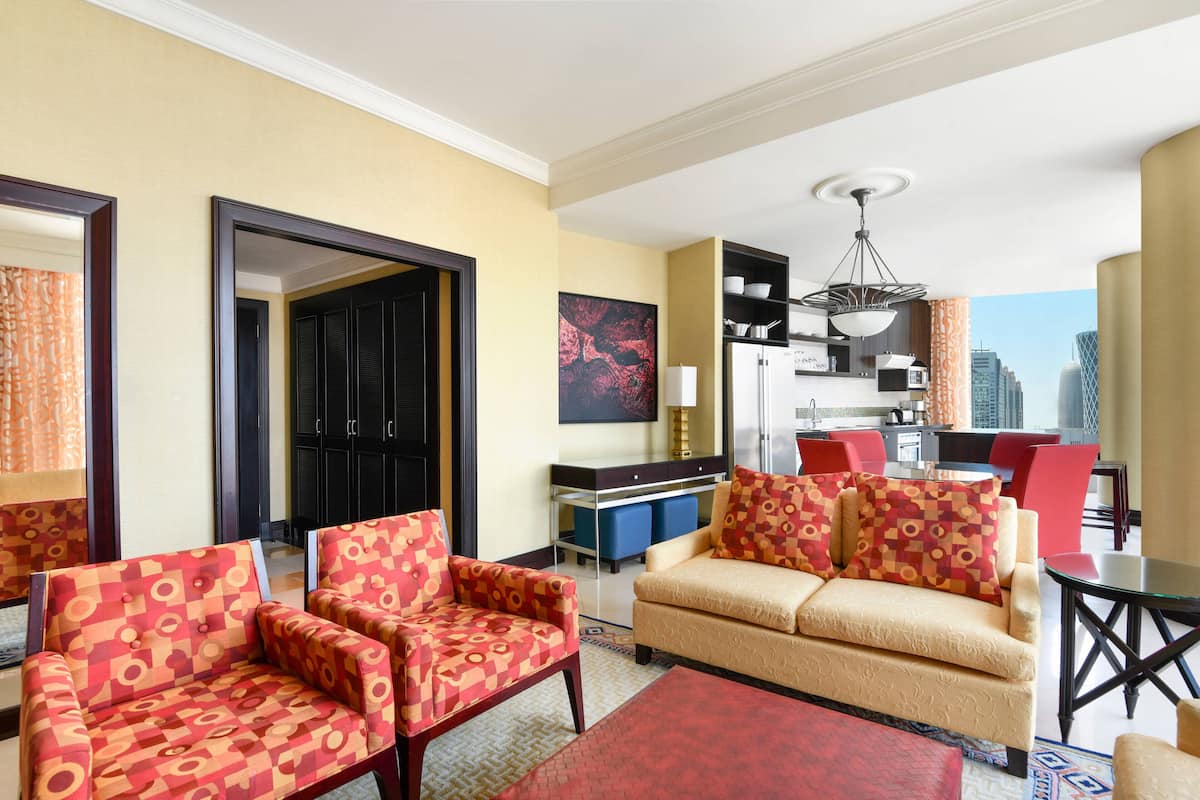 A hotel room with a living area featuring two sofas, a dining table, and a kitchen area with modern appliances.