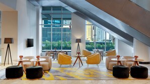 Un moderno vestíbulo de hotel con techo alto, ventanas amplias y una variedad de arreglos de asientos, incluyendo sofás y mesas redondas.
