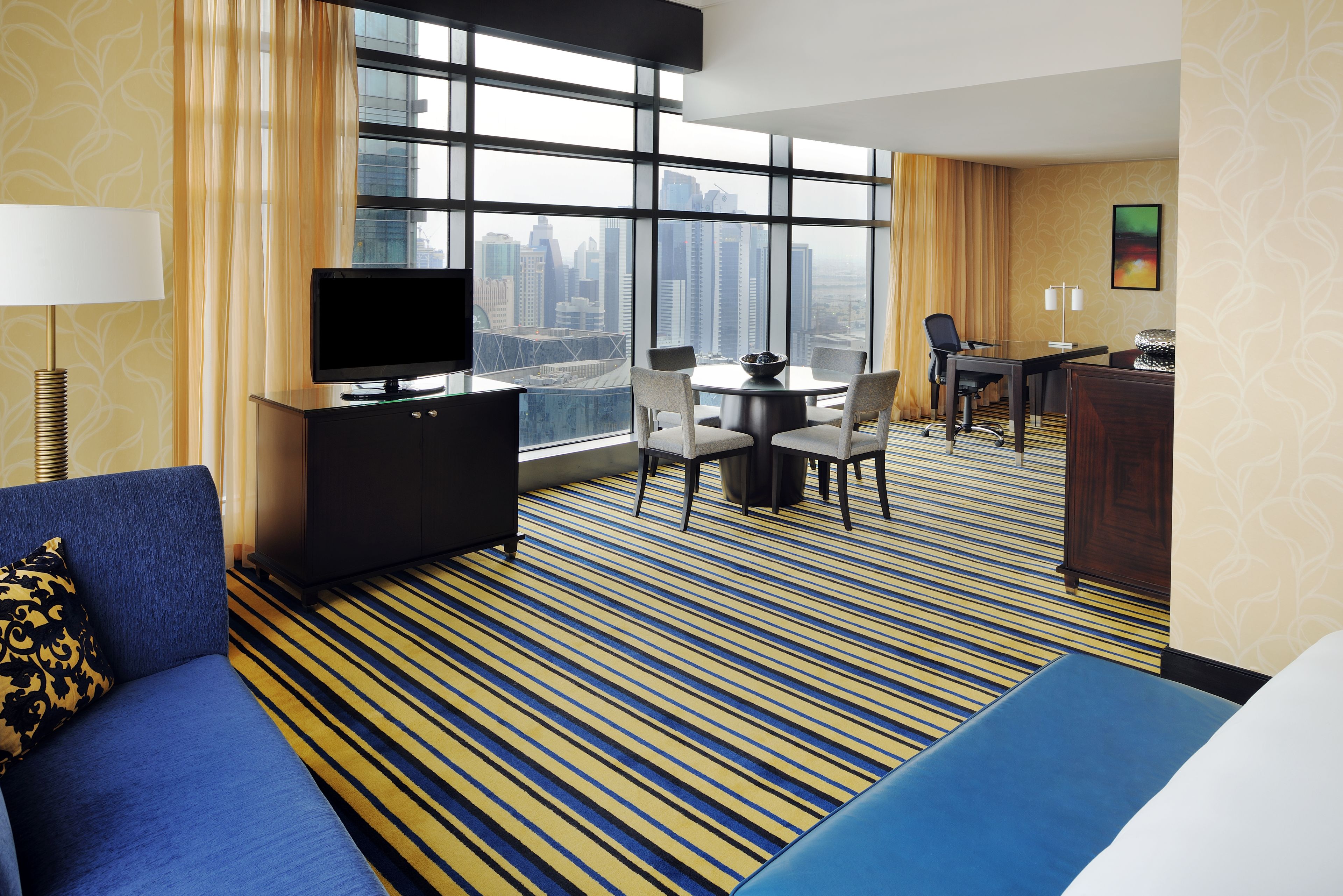 Une chambre d’hôtel dotée d’une grande fenêtre, d’un téléviseur à écran plat, d’un canapé, d’une table à manger avec des chaises et d’un bureau avec une chaise.