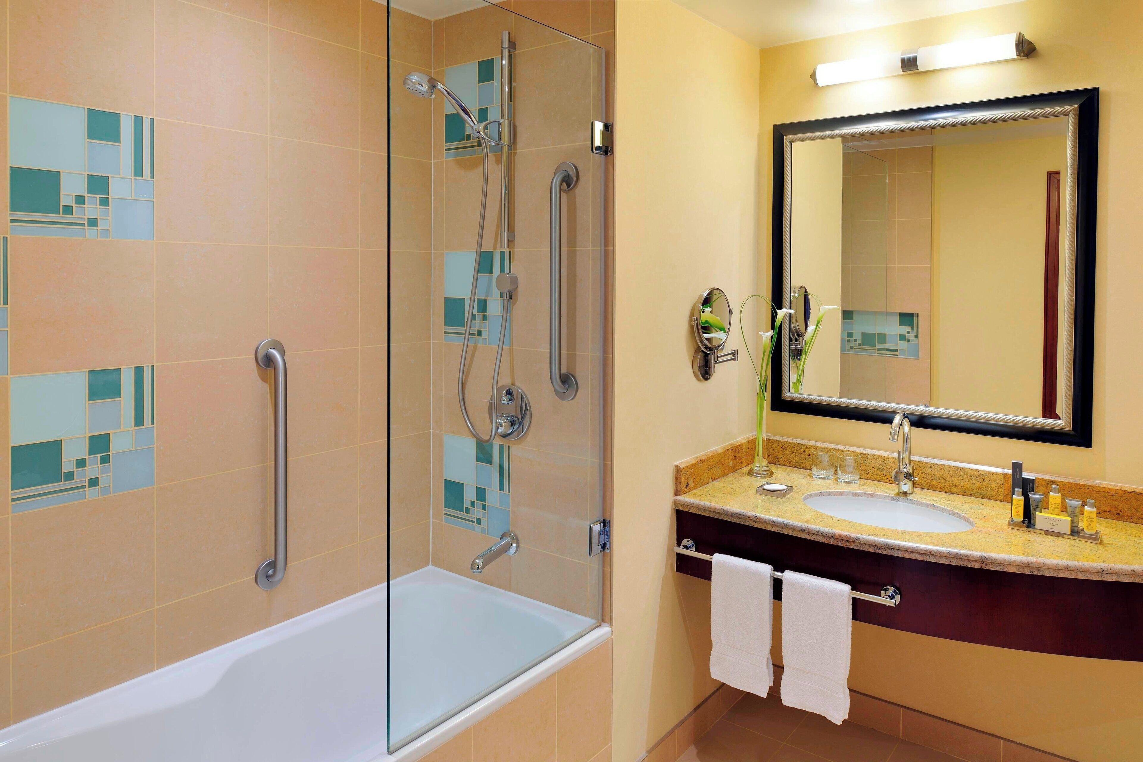 Une salle de bain avec une douche à parois de verre, une baignoire, un lavabo avec un miroir et un porte-serviettes.
