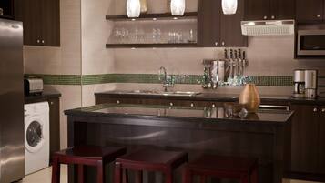 A modern kitchen with a central island, stainless steel appliances, and a green-tiled backsplash.