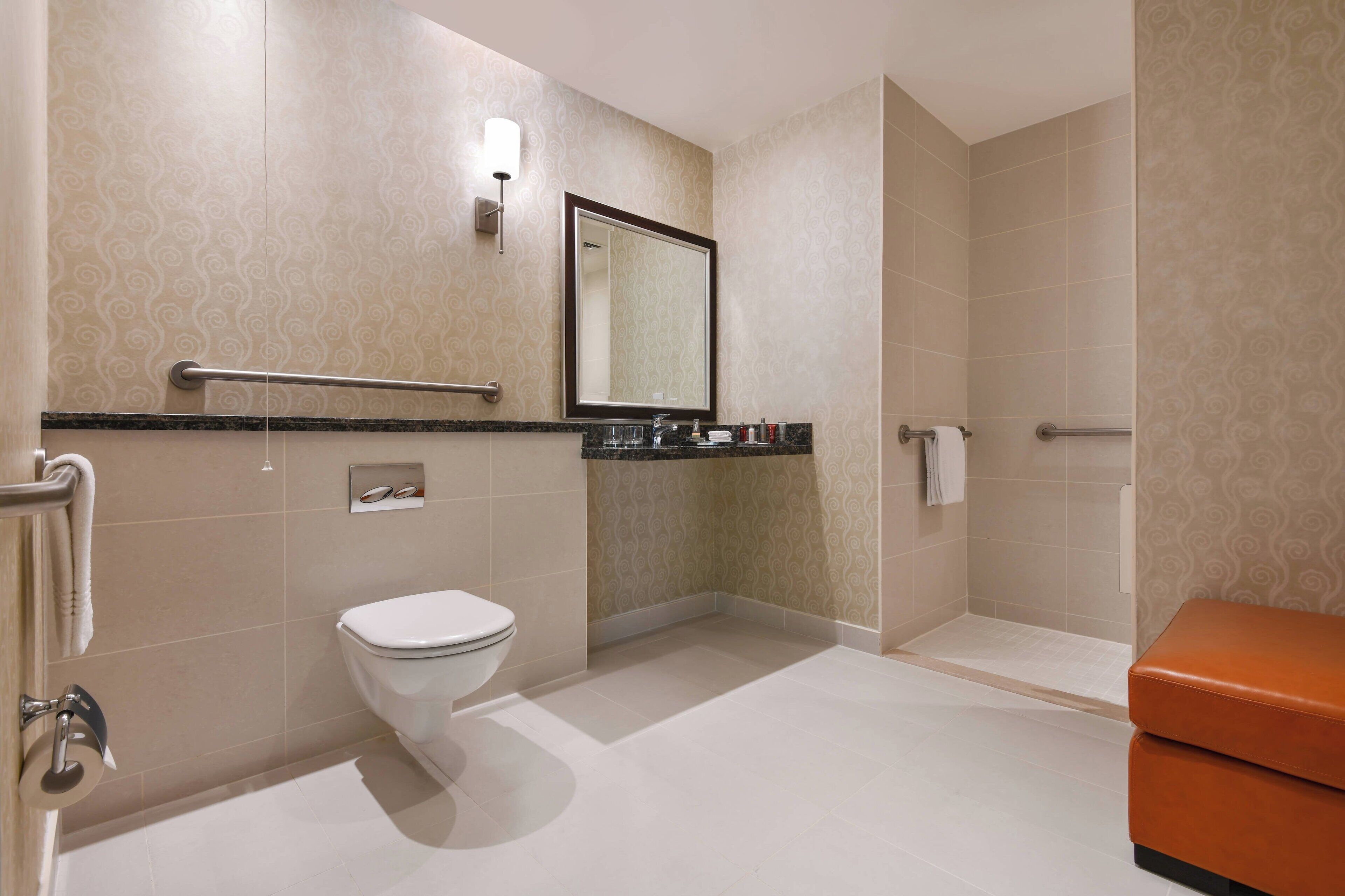 Un baño moderno con inodoro, lavamanos y zona de ducha, que presenta un diseño de baldosas estampadas y un espejo sobre el lavamanos.