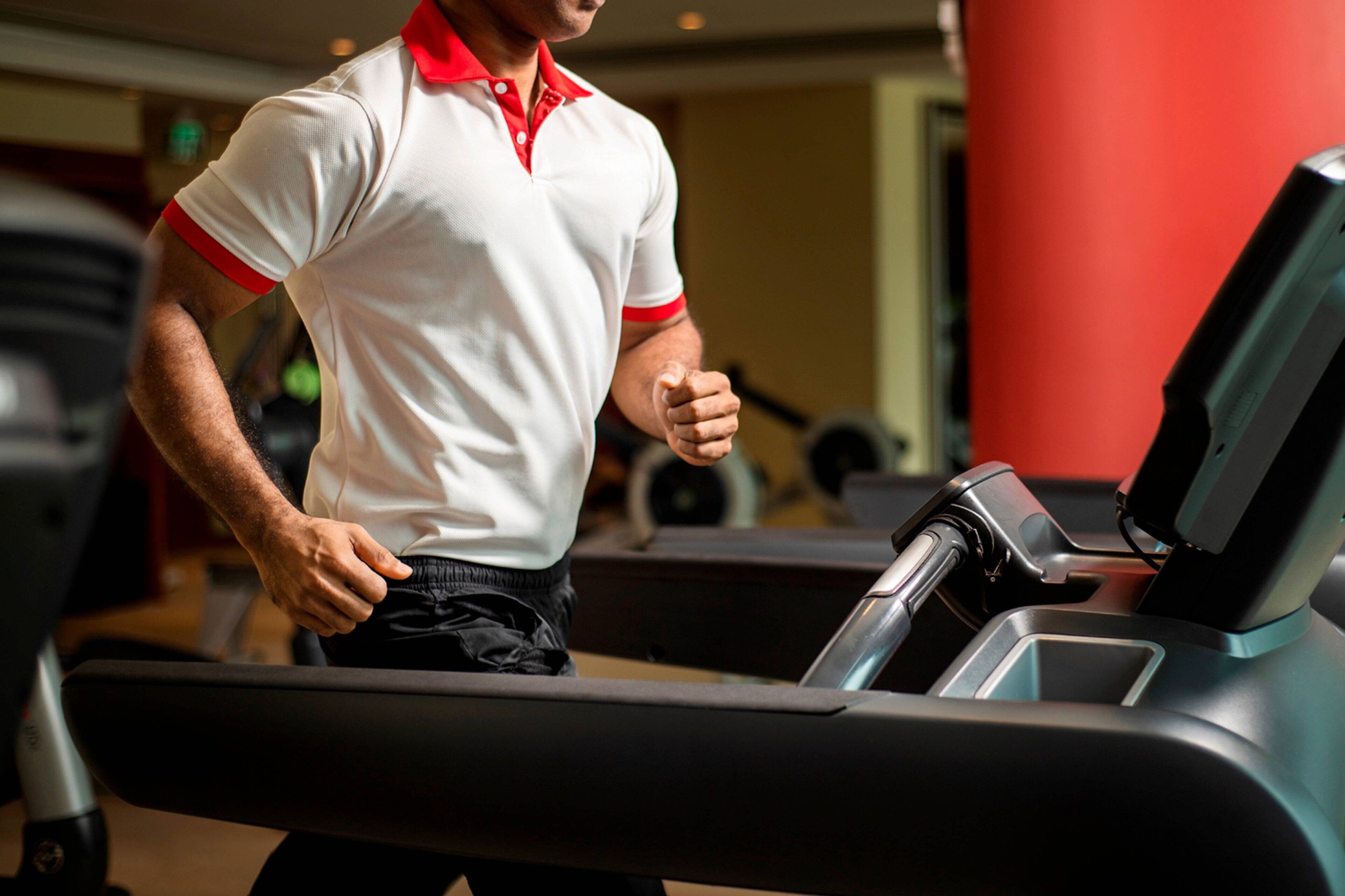 A man running on a treadmill in a gym with exercise equipment in the background.