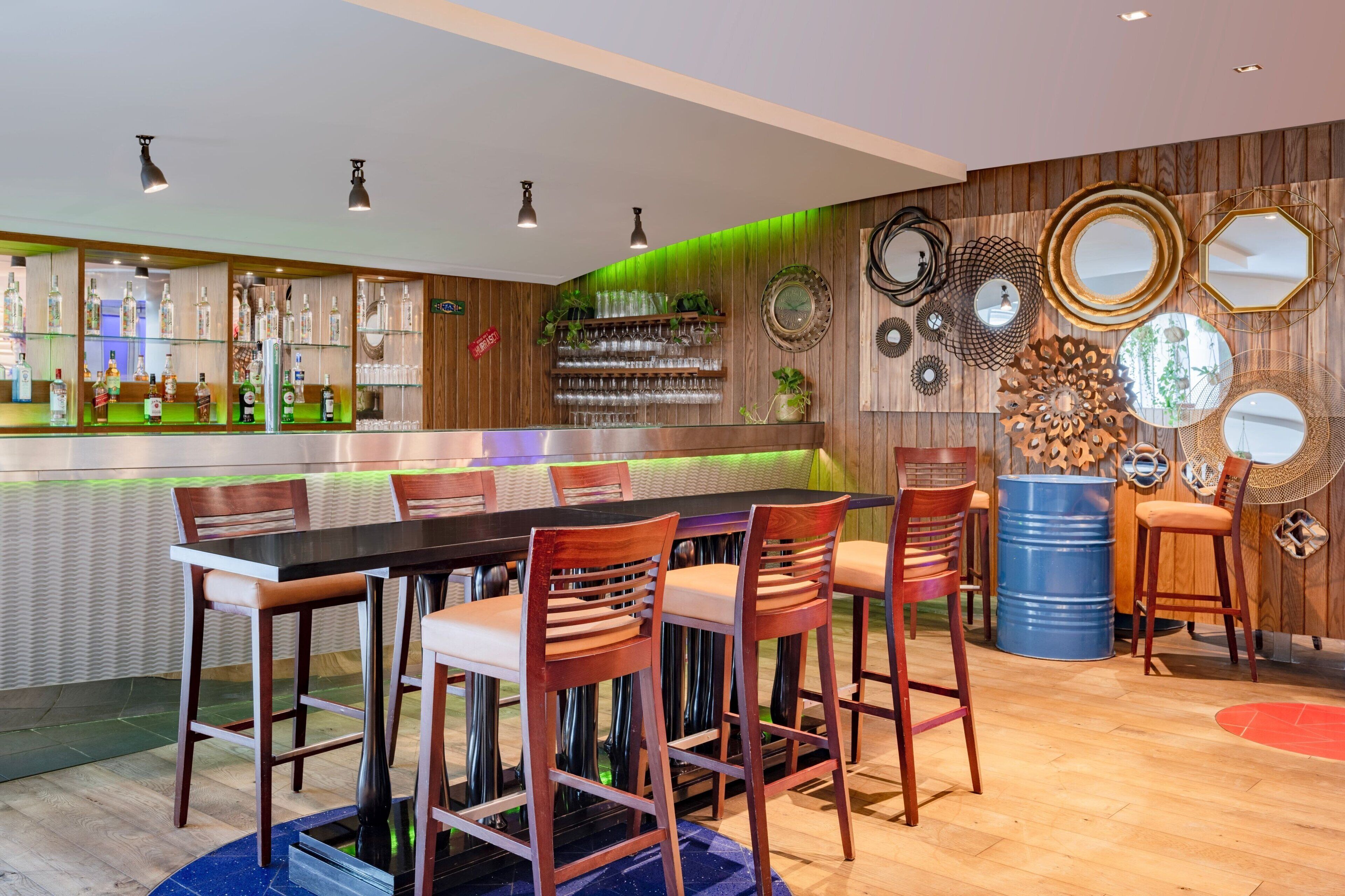 A bar area with a long counter, multiple stools, and a variety of decorative mirrors and wall art.