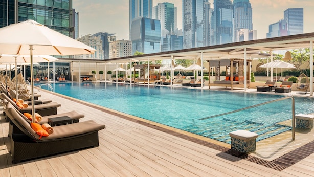 Piscina en la azotea con sillas de descanso y sombrillas, rodeada por el horizonte de una ciudad.