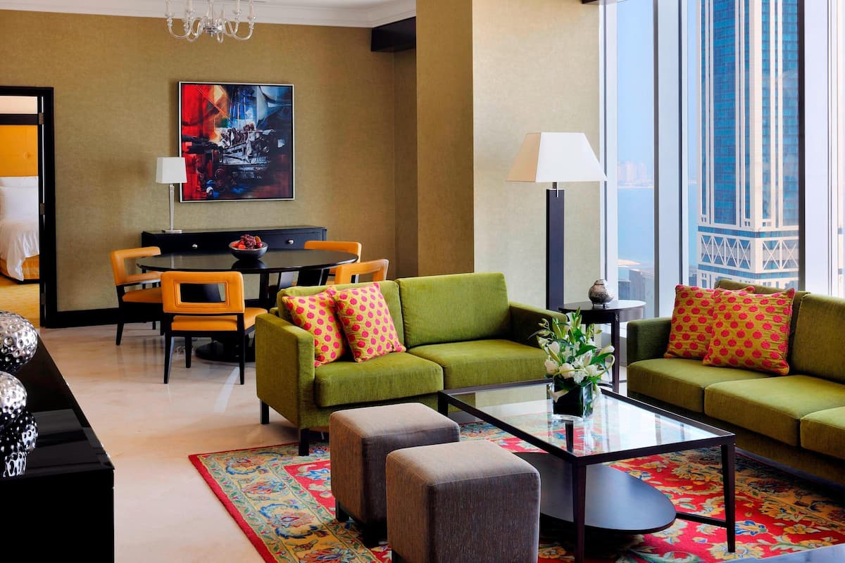 A modern living room with a green sofa, two ottomans, a coffee table, and a dining area with a table and chairs.