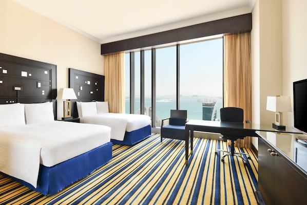 A hotel room with two beds, a desk, a chair, a TV, and a large window with a city view. - Marriott Marquis City Center Doha Hotel (Doha)