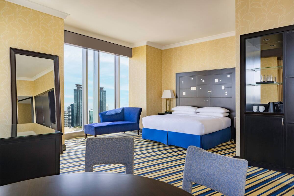 A hotel room with a large bed, a desk, a chair, a sofa, and a view of the city skyline.