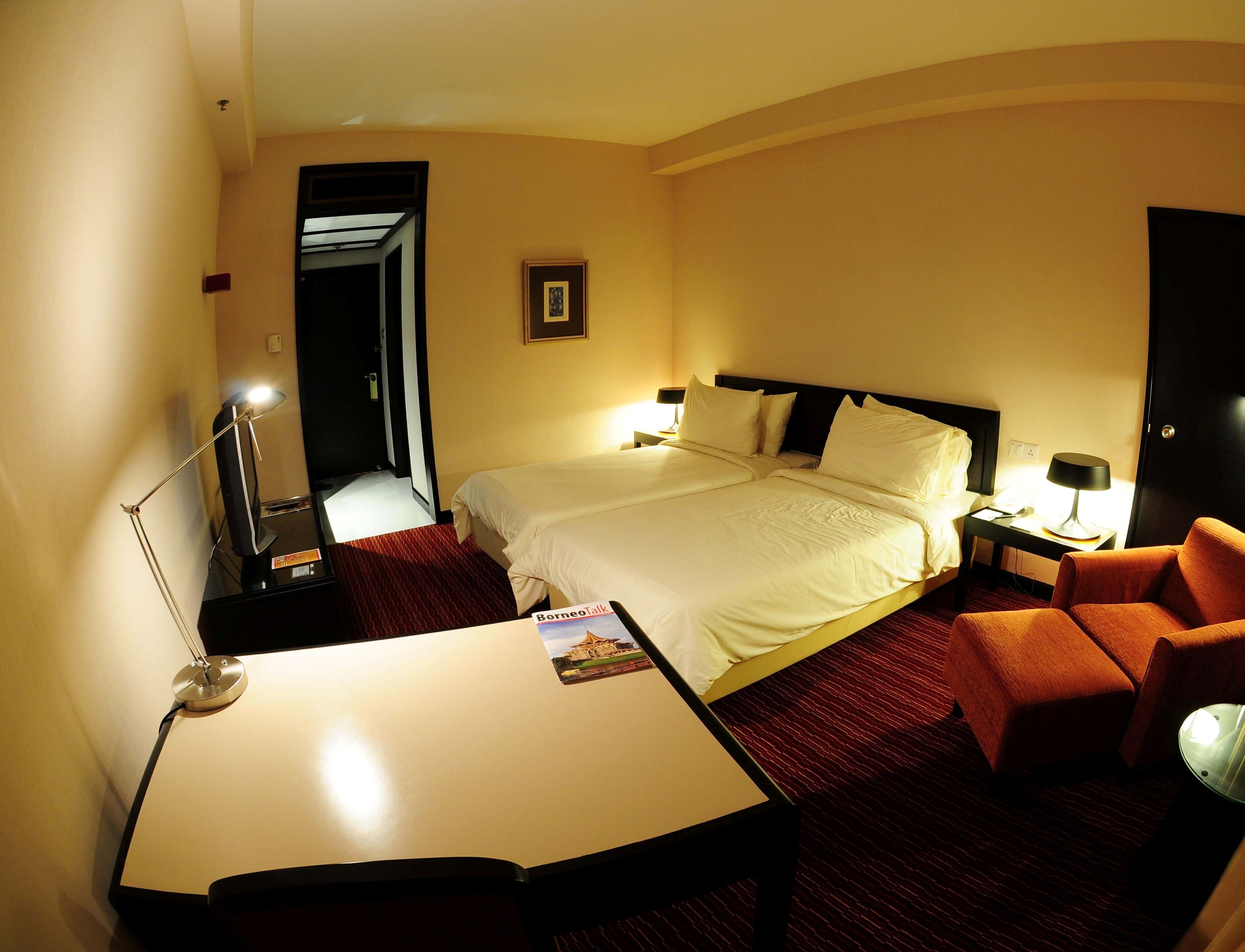 A hotel room with a bed, a desk, a chair, a lamp, and a framed picture on the wall.