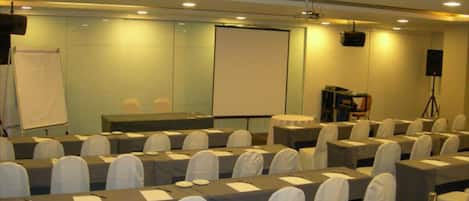A conference room with rows of tables and chairs, a projector screen, and a whiteboard.