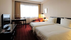 Een hotelkamer met twee bedden, een bureau, een televisie en een raam met gordijnen.