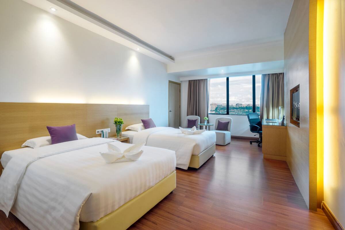 A hotel room with two beds, a desk, a chair, and a large window with a city view.
