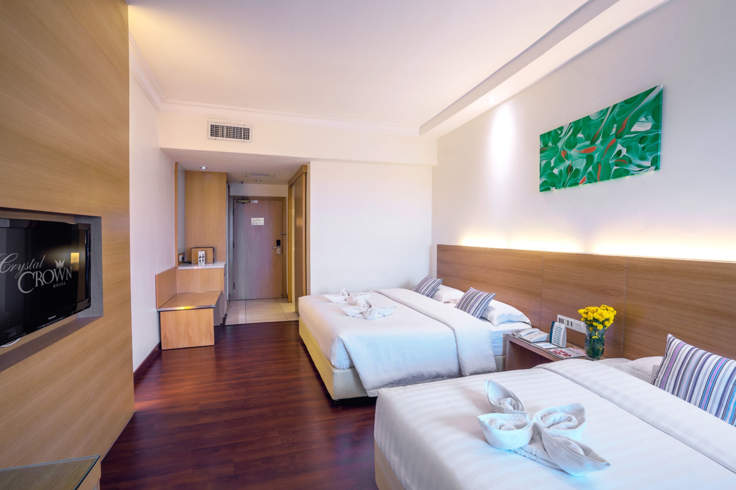 A hotel room with two beds, a TV, a wooden floor, and a green abstract painting on the wall.
