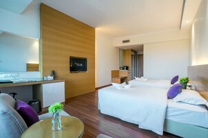A hotel room with a bed, a desk, a chair, a small table with a vase, and a trash bin.