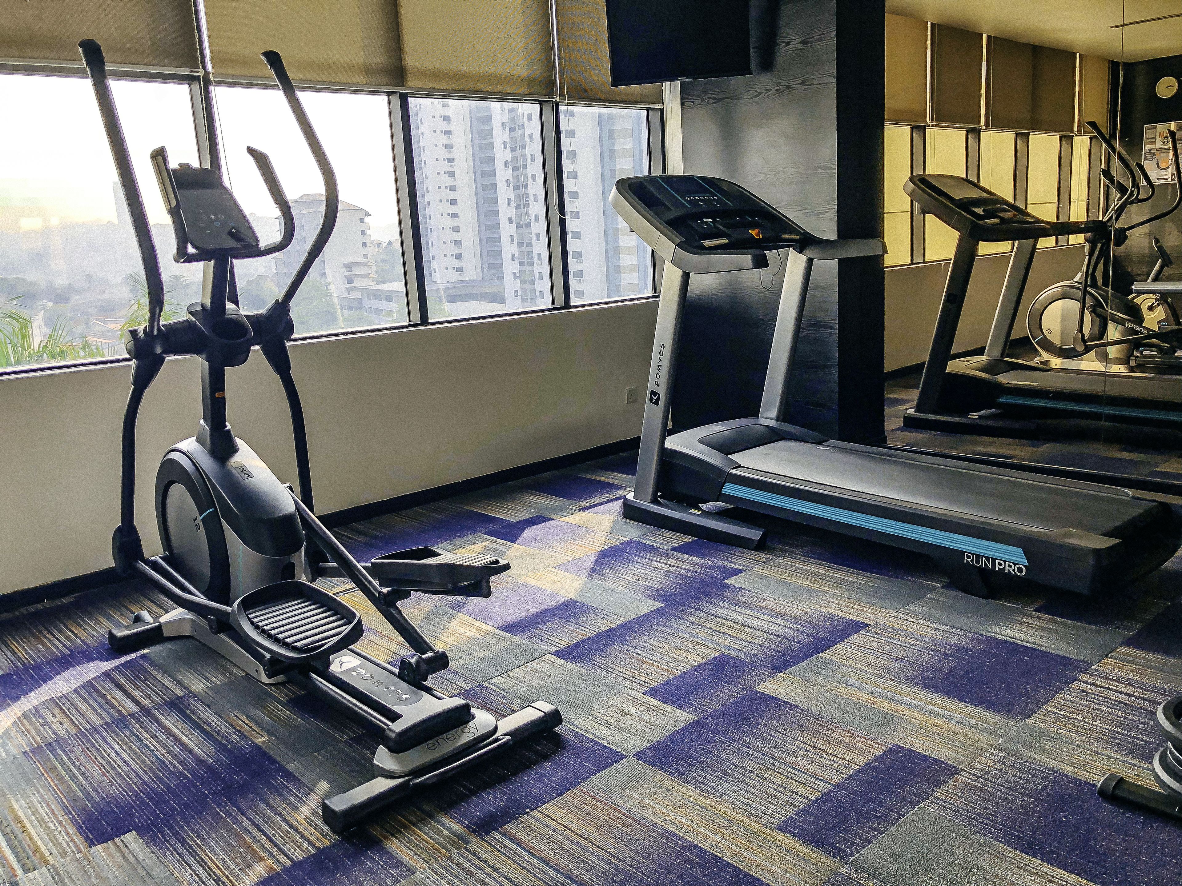 Ein Fitnessraum mit einem Crosstrainer, Laufband und einem gemusterten Teppich.