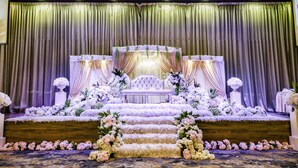 Un escenario con un sofá capitonado, cortinas drapeadas y arreglos florales.