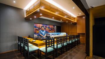 A restaurant with a long counter, multiple chairs, and a chef at the front.