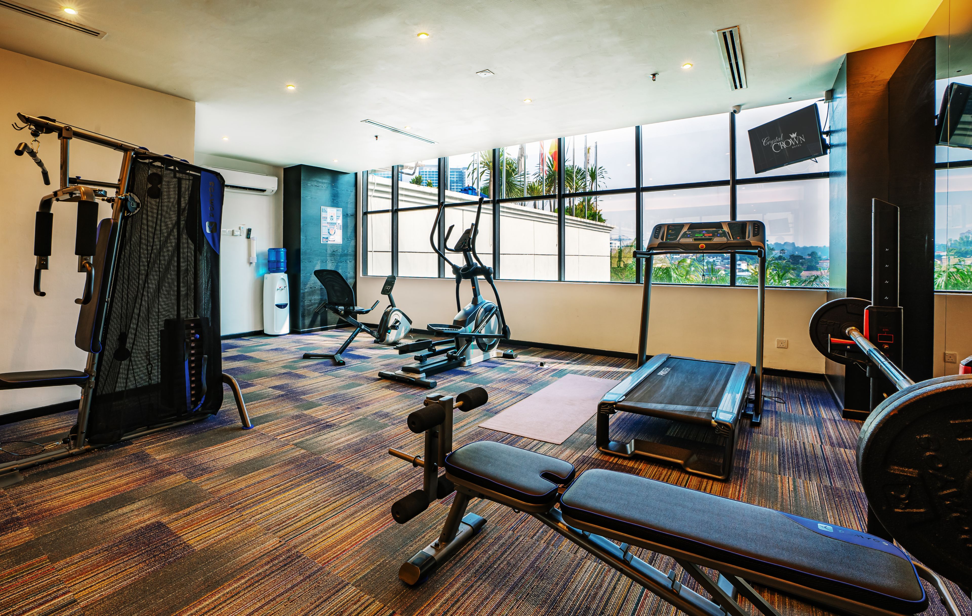 Un gimnasio con equipo de ejercicio, una banca y un ventanal con vista a palmeras.