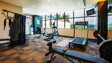 Un gimnasio con equipo de ejercicio, una banca y un ventanal con vista a palmeras.