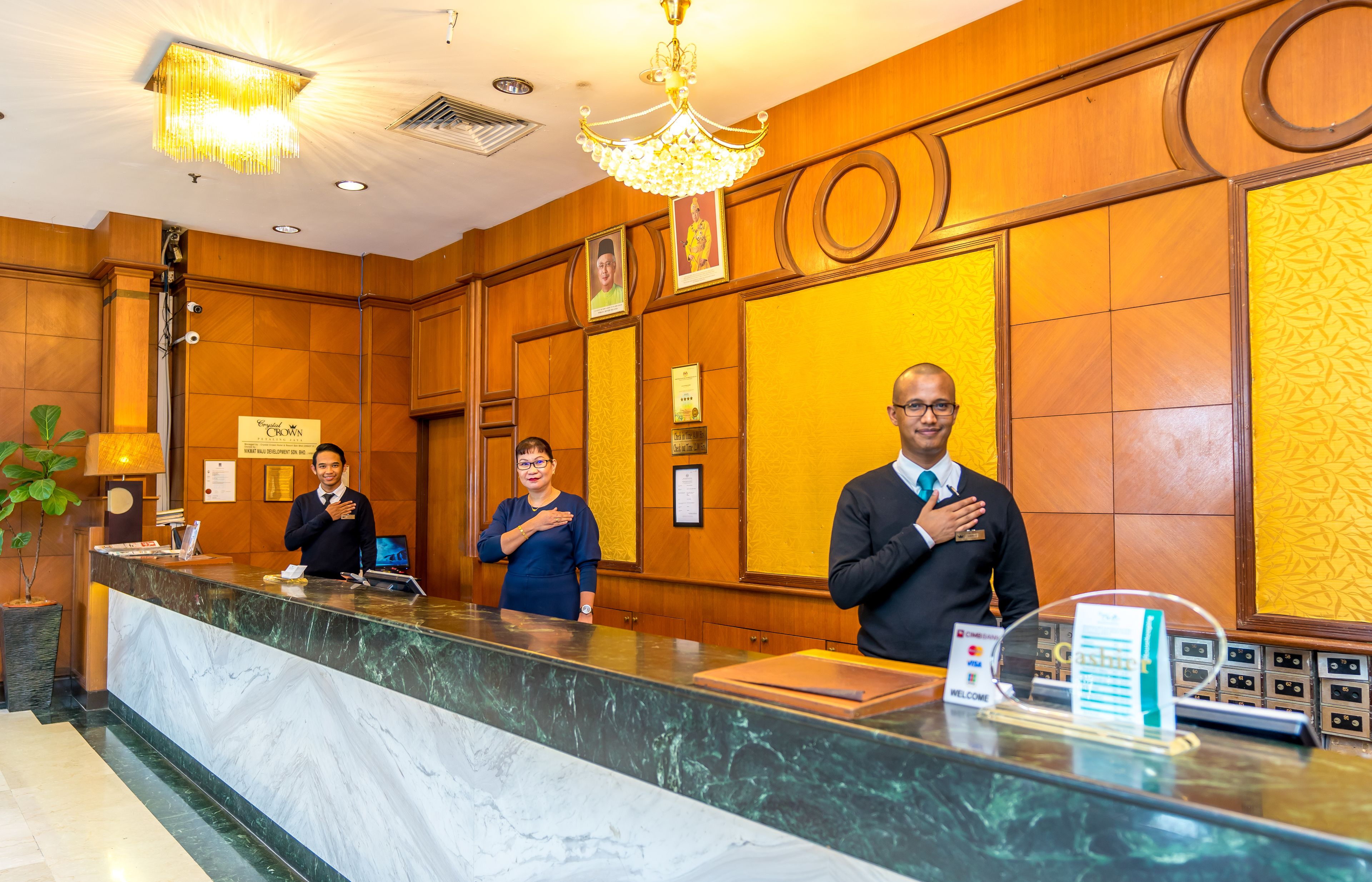 Uma área de recepção de hotel com balcão de mármore, painéis de madeira e um candelabro.