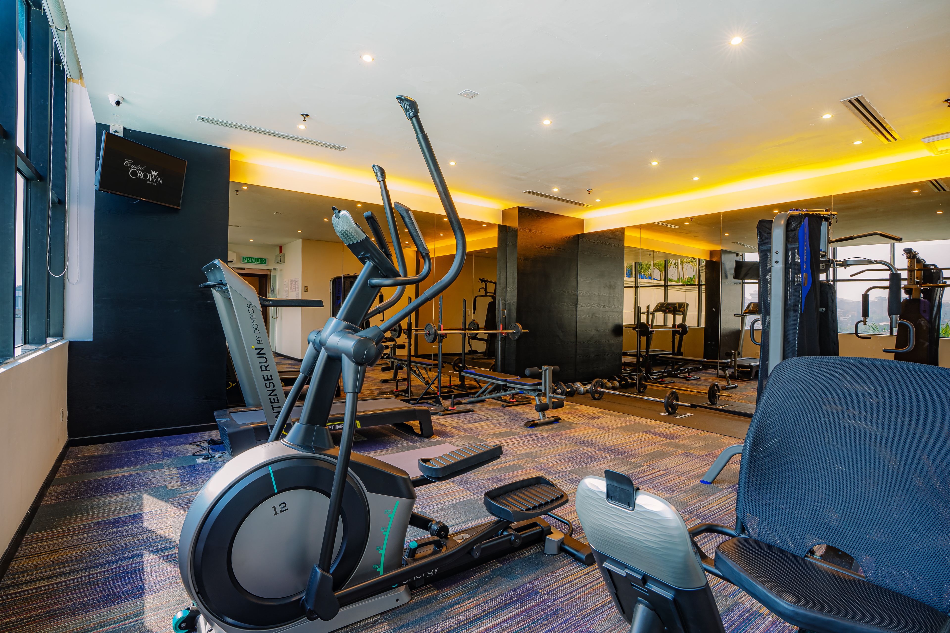 Ein Fitnessstudio mit unterschiedlichen Trainingsgeräten, darunter Laufbänder und Kraftgeräte, sowie einem großen Spiegel.