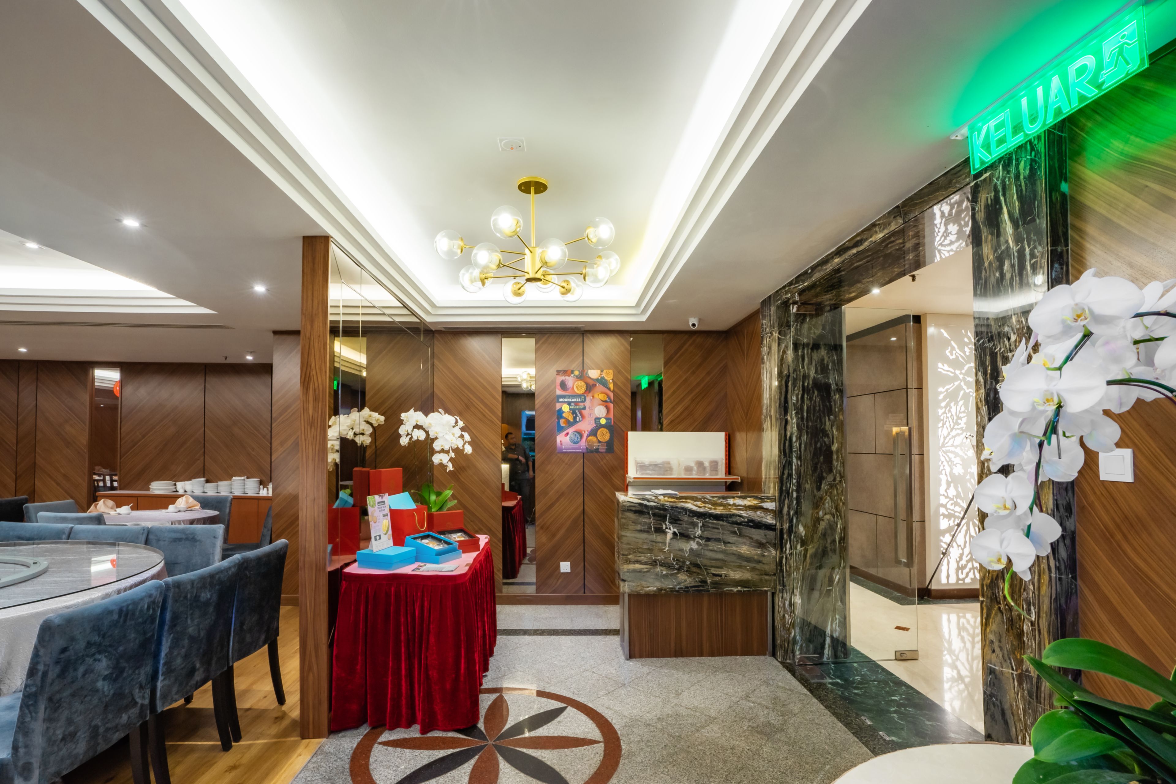 A hotel lobby with a reception desk, a chandelier, and a dining area with tables and chairs.