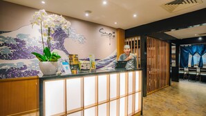 Un mostrador de recepción con un mural de paredes con diseño de olas, una orquídea en maceta y un atril para menús.