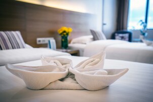 A hotel room with two beds, a bedside table with a vase of yellow flowers, and a wall-mounted light fixture.
