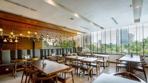 Un restaurante moderno con mesas y sillas de madera, techo alto y ventanas amplias que ofrecen vistas a la ciudad.
