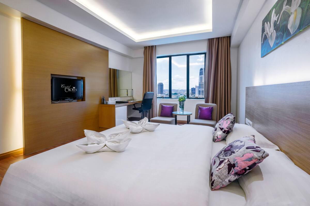 A hotel room with a large bed, a desk, a chair, a small table, and a TV on the wall.