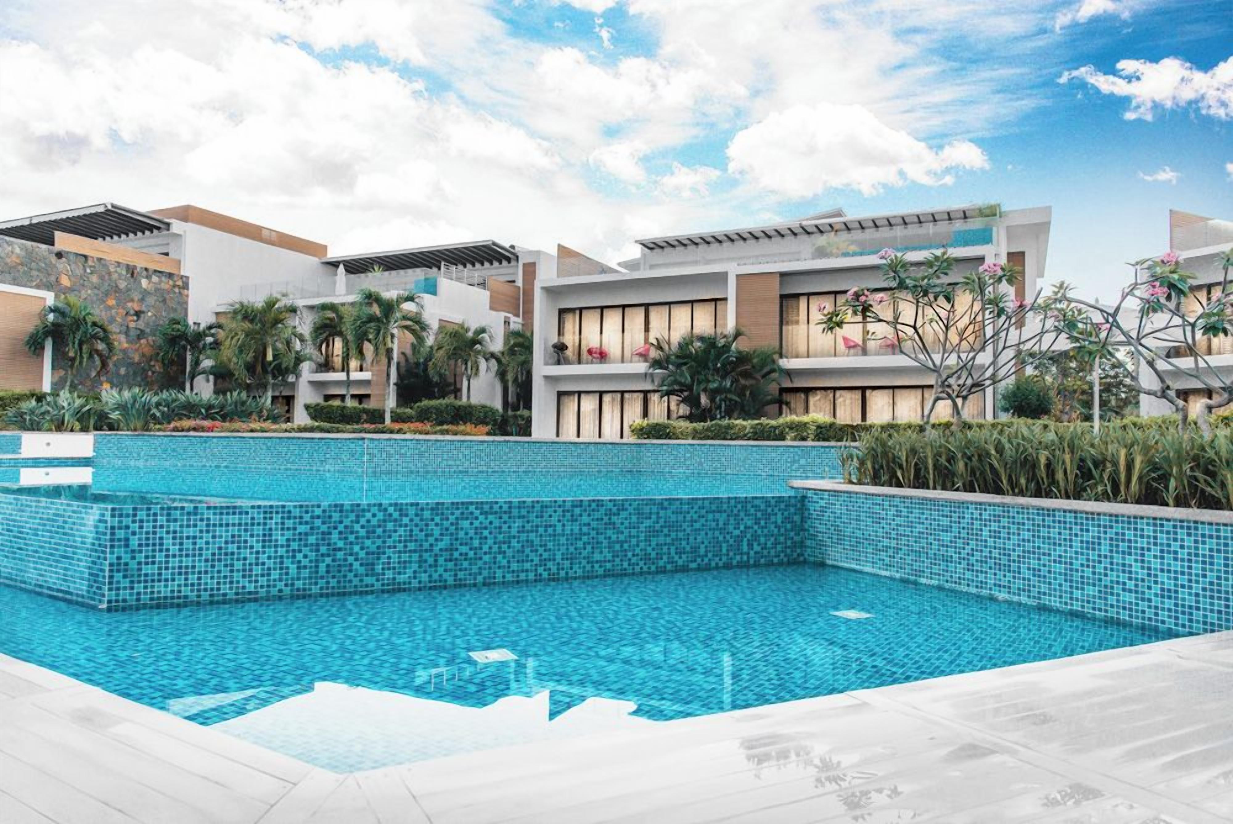 A modern hotel with a swimming pool, palm trees, and a clear sky.