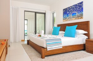 A hotel room with a bed, a wooden headboard, a painting on the wall, and a view through the window. - Cap Ouest by Dream Escapes (Flic-en-Flac)