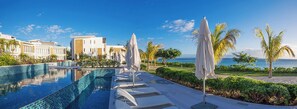 A resort pool area with a clear view of the sea, palm trees, and modern buildings. - Cap Ouest by Dream Escapes (Flic-en-Flac)