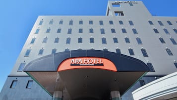 A hotel building with a prominent sign reading "APA HOTEL" and "KAGOSHIMA - KOKUBU".