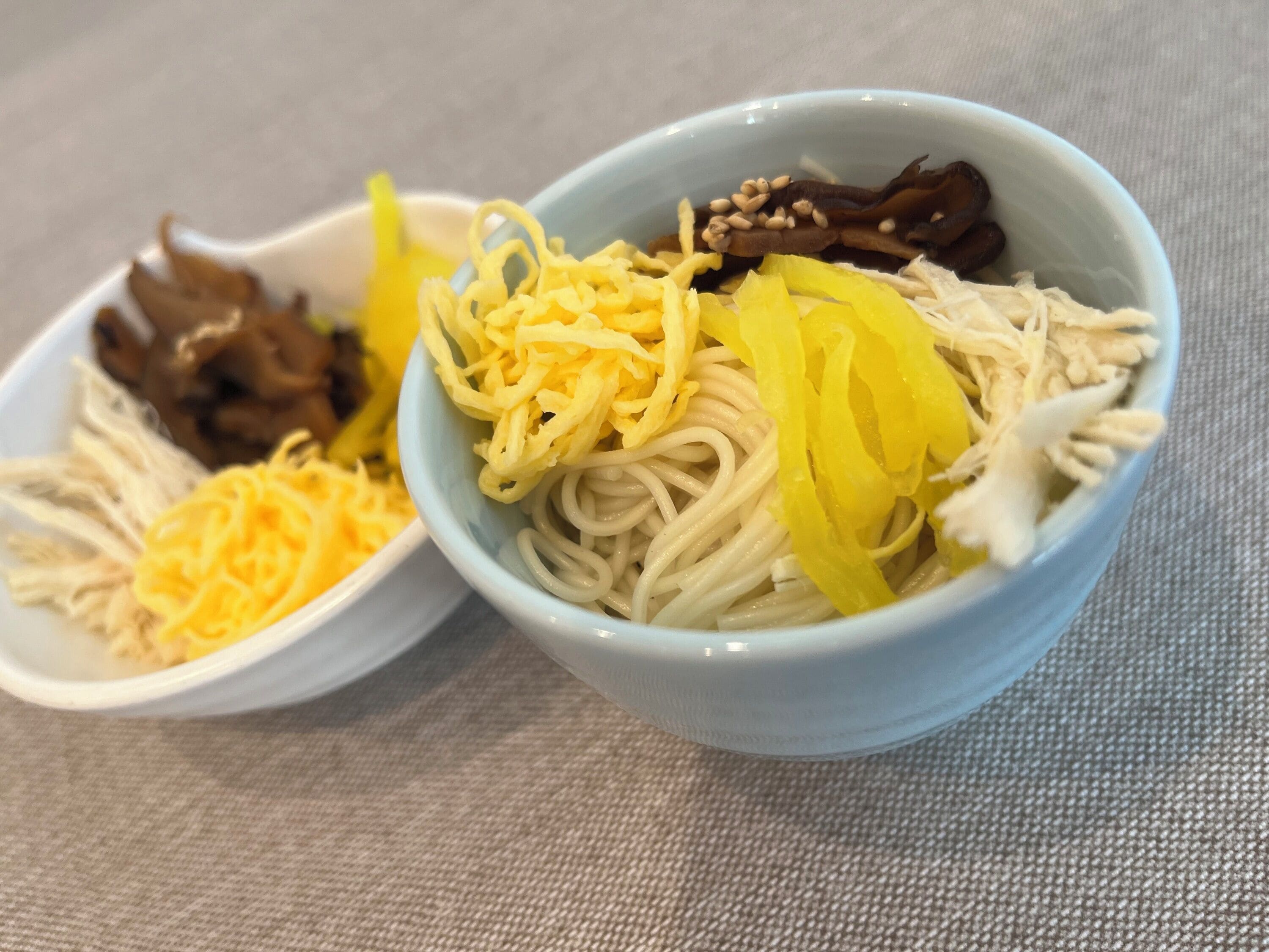 Two bowls of noodles with various toppings.