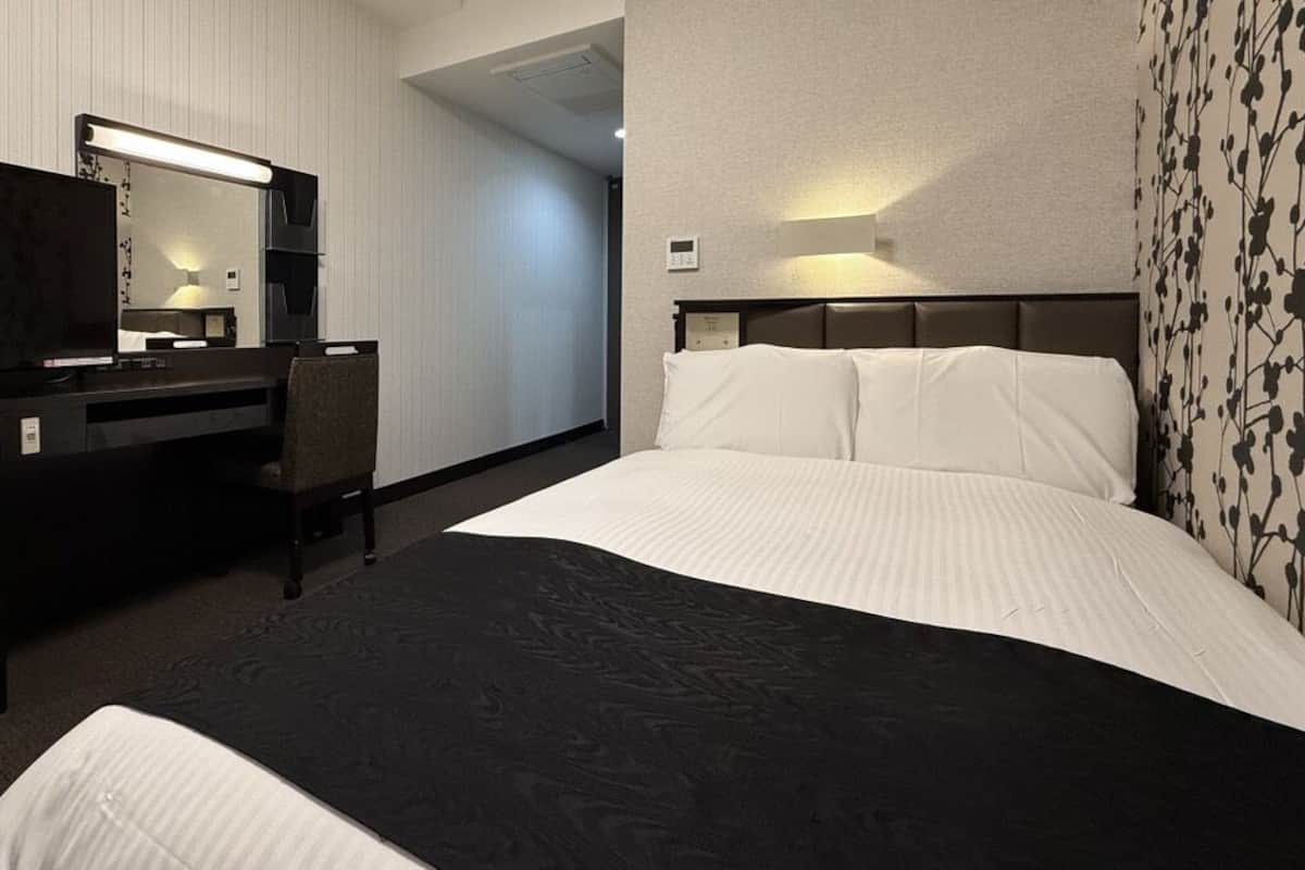 Una habitación de hotel con una cama, un escritorio, una silla, un televisor y un espejo.