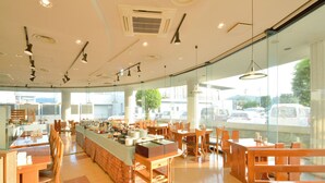 A spacious restaurant with a long counter, multiple tables, and a large window offering a view of the street. - APA Hotel Kagoshima Kokubu (Kirishima)