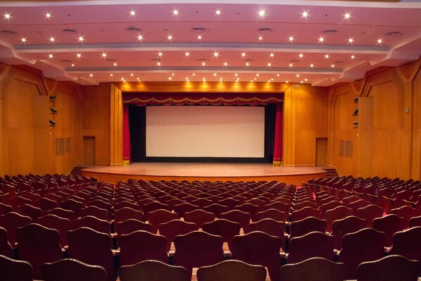 A theater with rows of red seats, a stage with a red curtain, and a large screen. - Tolip Aswan Hotel (Aswan)